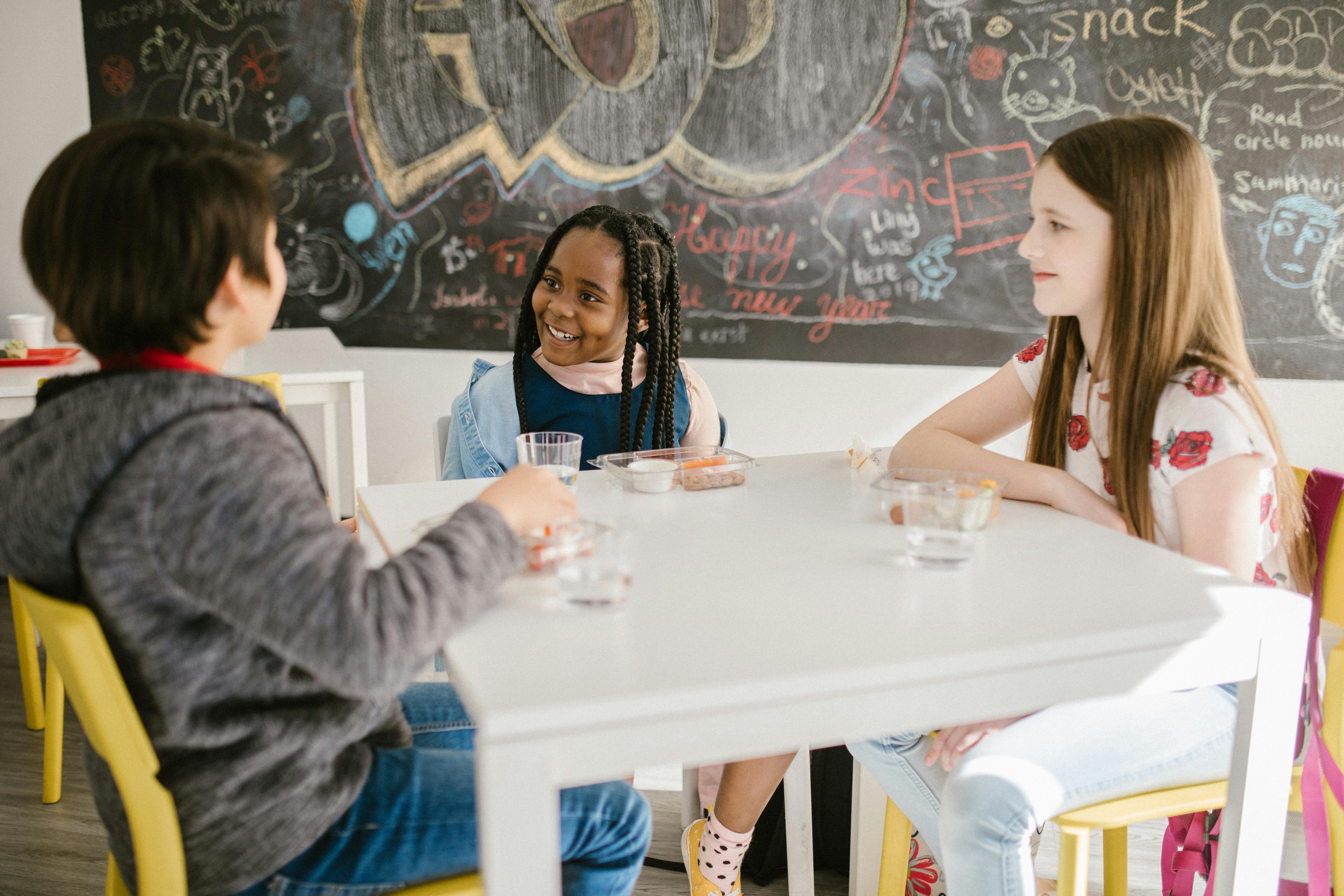 Children laughing together with snacks and drinks during free breakfast club activities in classroom
